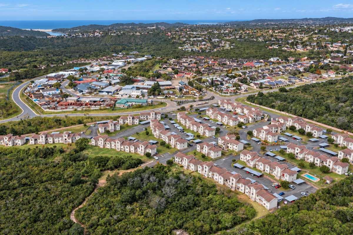 Aerial view of a residential townhouse complex featuring multiple units, paved parking areas, carports, and a communal swimming pool set within a natural landscape.