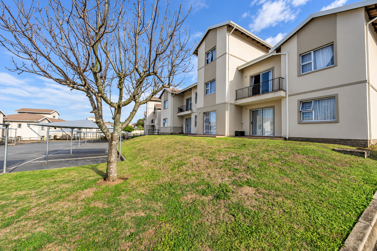 Rear view of a townhouse complex featuring a grassy lawn, private balconies with metal railings, sliding glass doors, and adjacent covered parking bays.