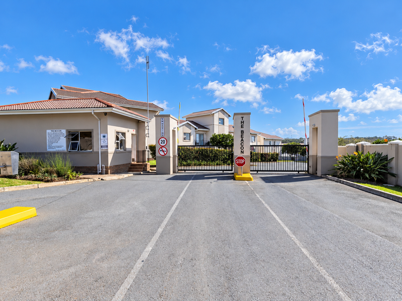 The secure entrance to The Beacon townhouse complex, featuring a gated access point, guard house, and well-maintained paved driveway.