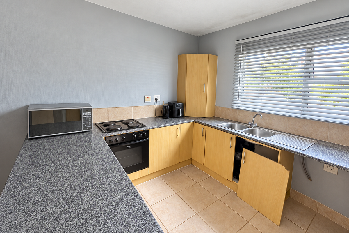 A functional kitchen featuring laminate countertops, built-in oven and hob, tiled splashback, and light wood veneer cabinetry with some visible maintenance required.