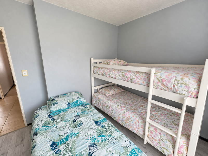 A functional bedroom featuring light grey walls and durable laminate flooring, currently configured with bunk beds and a single bed.