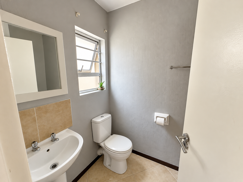 A clean and functional guest bathroom featuring a pedestal washbasin, toilet, tiled flooring, and a neutral grey wall finish.