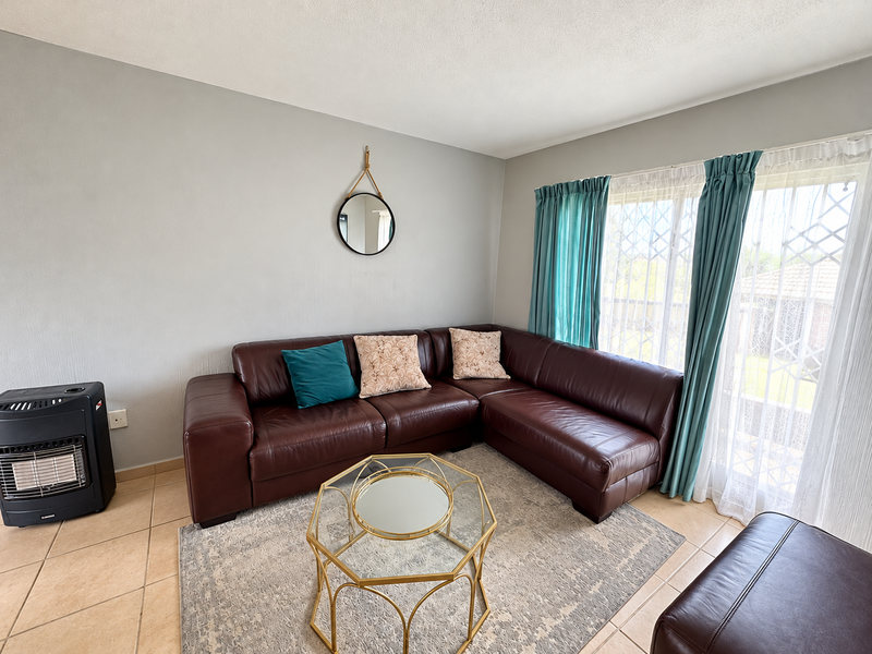 A bright living room featuring tiled flooring and a large sliding glass door with security gate, providing access to the exterior.