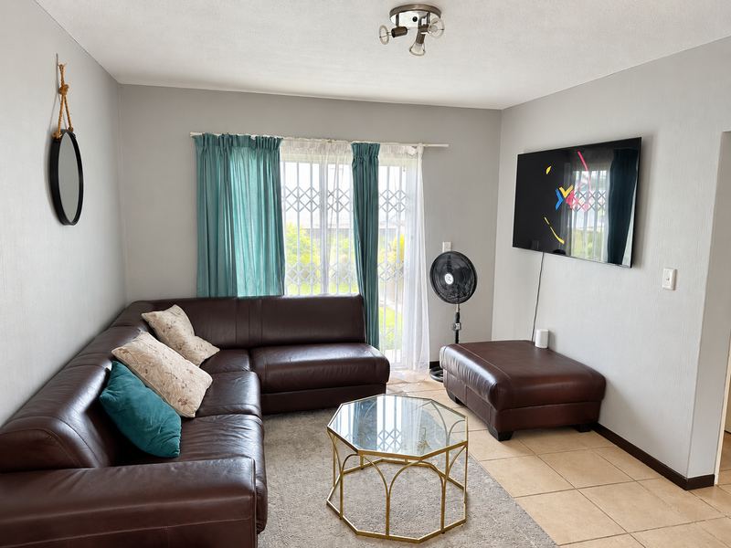 A comfortable living room featuring tiled flooring, neutral wall tones, and a security gate leading to the exterior.