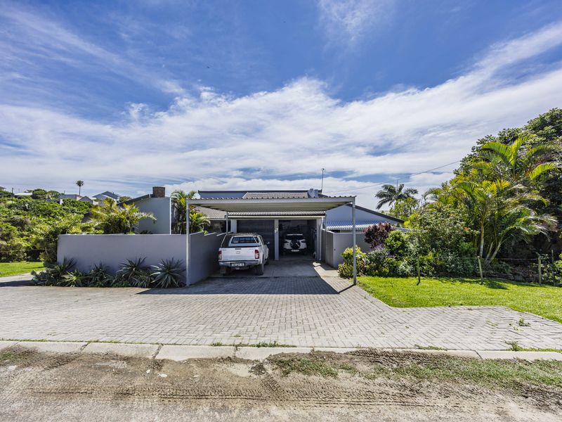 Front view of the property featuring a paved driveway, a covered carport, and a double garage with surrounding landscaped garden and boundary wall.