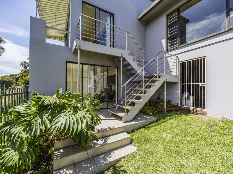 Rear exterior view featuring a tiled patio, external staircase with stainless steel balustrades, and access to the lower level via sliding glass doors.