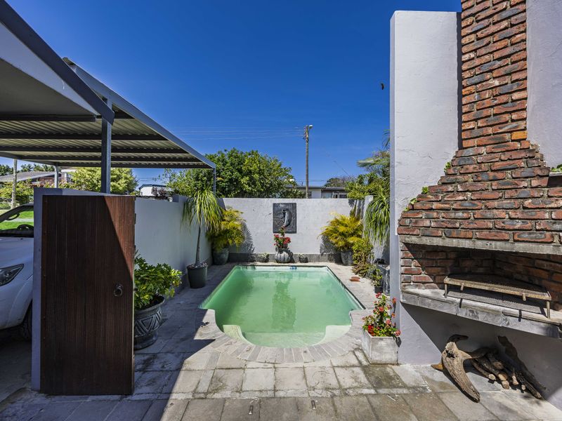 Outdoor entertainment area featuring a swimming pool, built-in brick braai, and a covered carport, set within a private walled courtyard.