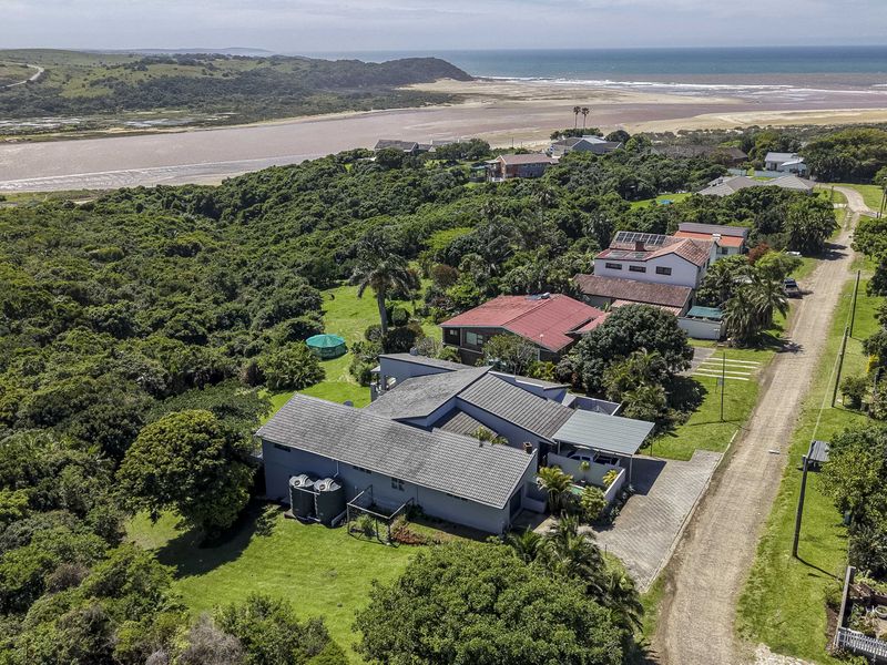 Aerial view of the property showcasing the roof structure, water tanks, driveway, and surrounding coastal landscape.