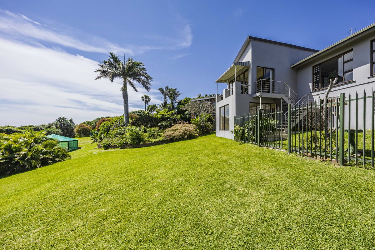 A well-maintained rear exterior view of the property featuring a spacious lawn, landscaped garden, and an elevated balcony with external staircase access.