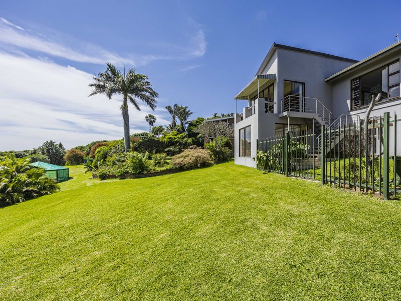 A well-maintained rear exterior view of the property featuring a spacious lawn, landscaped garden, and an elevated balcony with external staircase access.