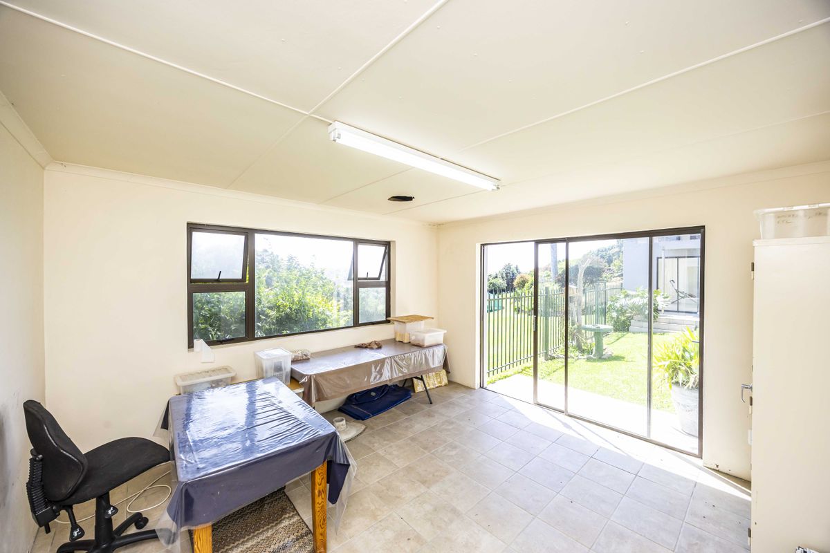 A bright, open-plan living space featuring tiled flooring, large aluminium windows, and sliding glass doors providing direct access to the garden.