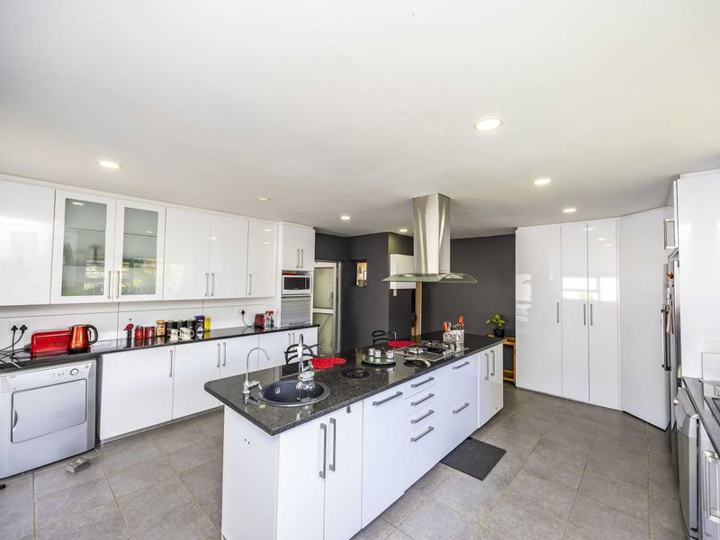 Modern kitchen featuring a central island with stone countertops, sleek white cabinetry, stainless steel extractor fan, and integrated appliances with tiled flooring.