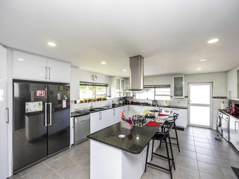 Spacious modern kitchen featuring a large central island with gas hob, granite countertops, ample white cabinetry, and integrated stainless steel extractor fan.