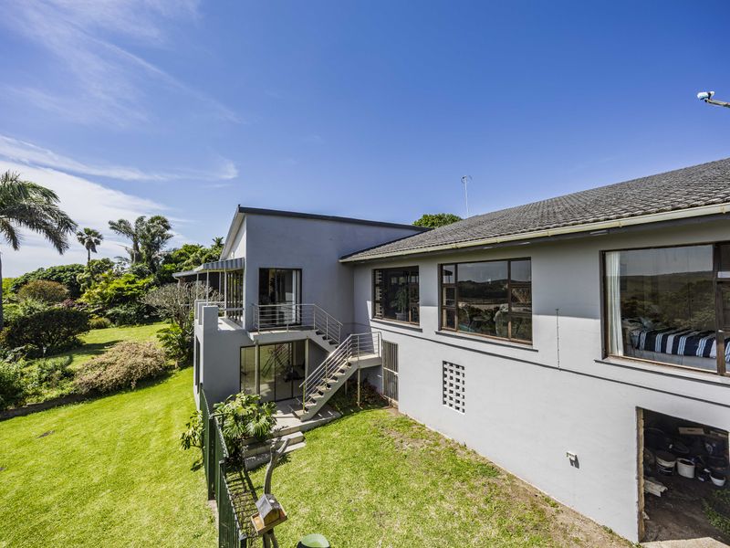 Rear view of the property featuring a multi-level exterior with a metal staircase, large windows, and a spacious landscaped garden.