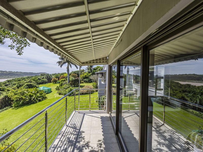 A spacious covered balcony featuring tiled flooring, a stainless steel balustrade, and large sliding glass doors with scenic garden and landscape views.