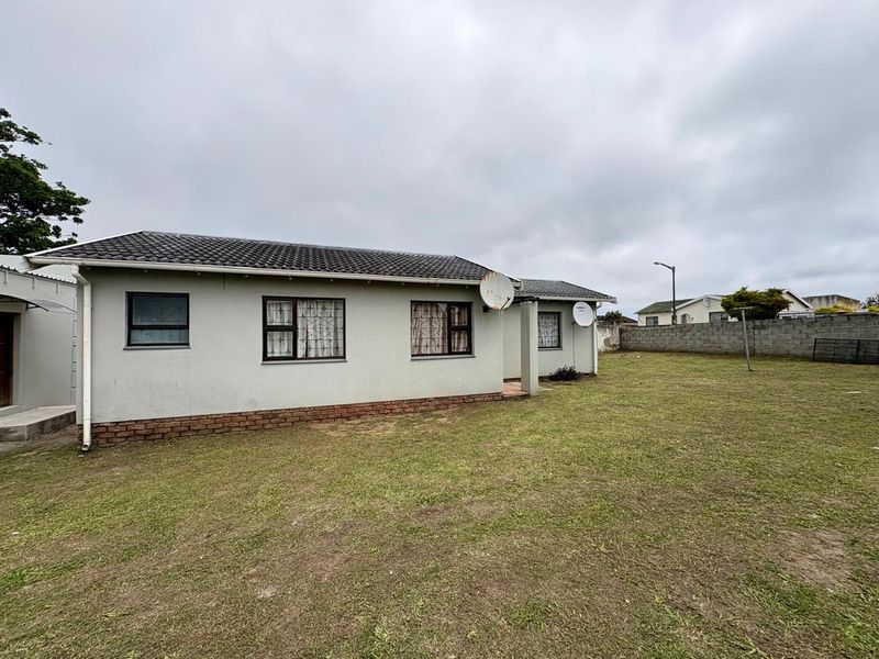 Rear view of the house featuring a tiled roof, brick plinth, and a spacious backyard enclosed by a concrete boundary wall.