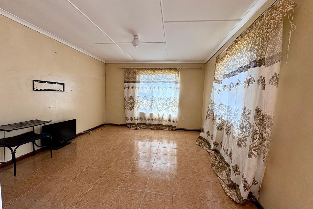 A spacious, empty living room featuring tiled flooring, a ceiling fan, and neutral wall tones, offering a blank canvas for personalization.