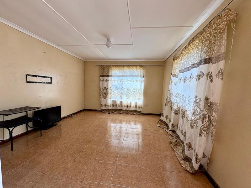 A spacious, empty living room featuring tiled flooring, a ceiling fan, and neutral wall tones, offering a blank canvas for personalization.