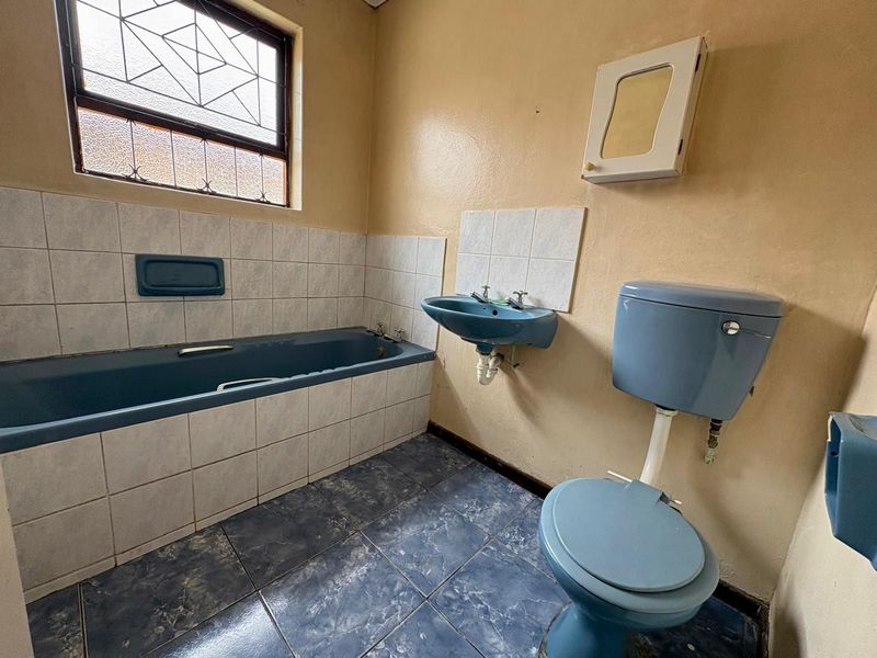 A dated bathroom featuring a blue suite, tiled flooring, and tiled splashbacks, offering significant potential for a modern renovation.