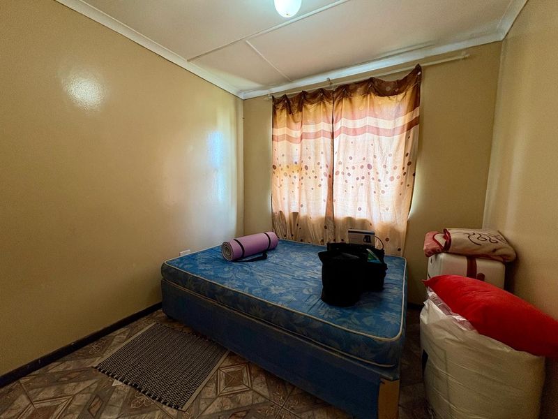 A compact bedroom featuring tiled flooring and a window with curtain fixtures, offering a functional space ready for cosmetic updates and modernization.