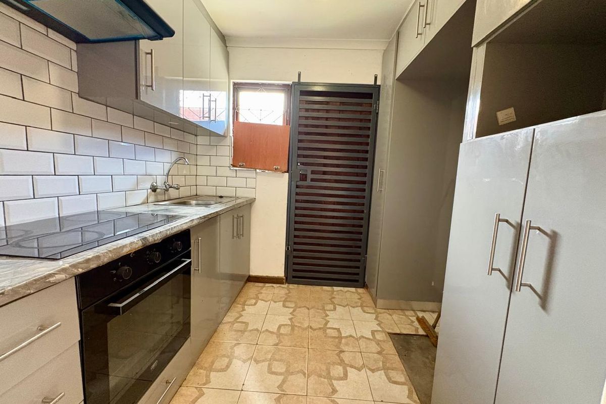 A functional kitchen featuring modern grey cabinetry, a built-in oven and hob, subway tile backsplash, and direct access to an exterior security gate.