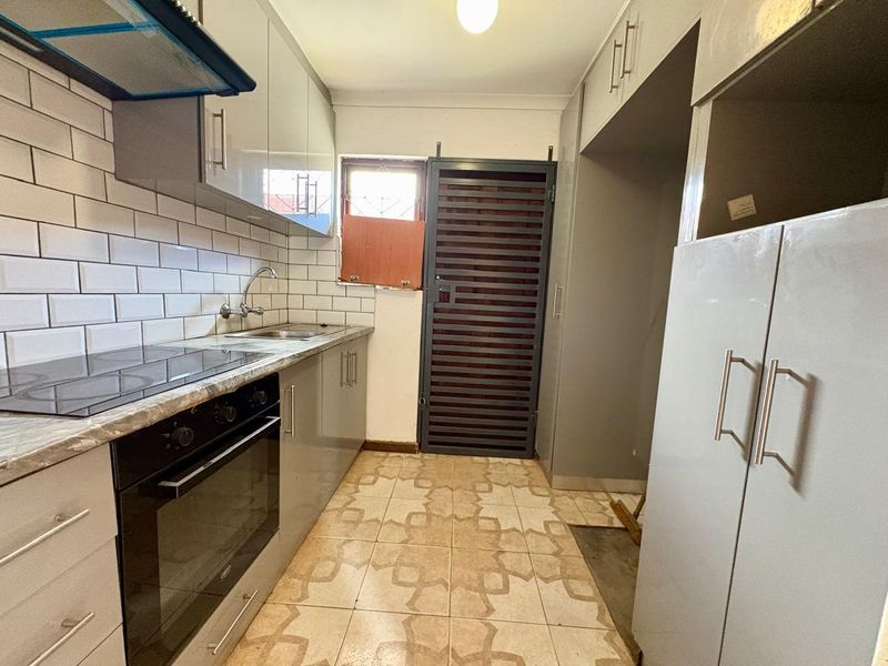 A functional kitchen featuring modern grey cabinetry, a built-in oven and hob, subway tile backsplash, and direct access to an exterior security gate.