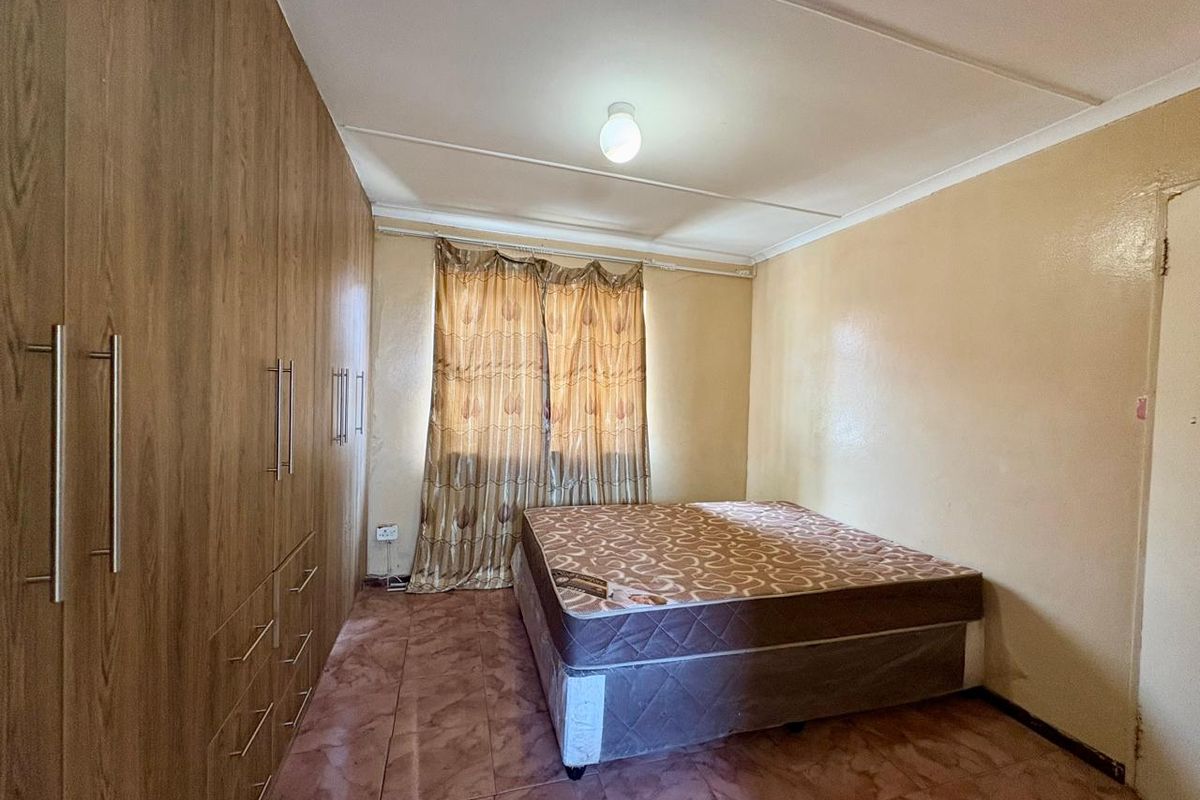 A bedroom featuring built-in wooden cupboards, tiled flooring, and a coved ceiling. The room requires cosmetic updates to improve its overall condition.