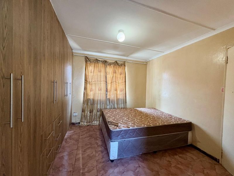 A bedroom featuring built-in wooden cupboards, tiled flooring, and a coved ceiling. The room requires cosmetic updates to improve its overall condition.