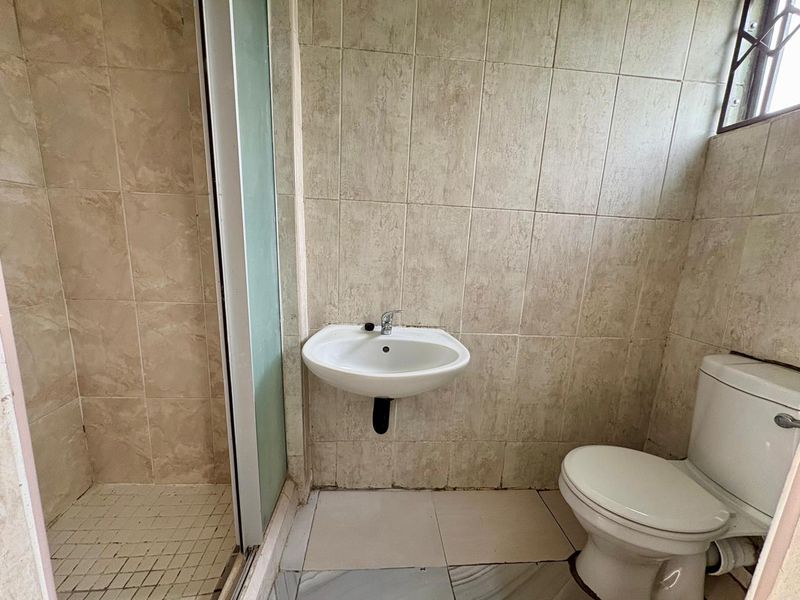A compact bathroom featuring a shower enclosure, wall-mounted basin, and toilet, finished with neutral ceramic tiling throughout.