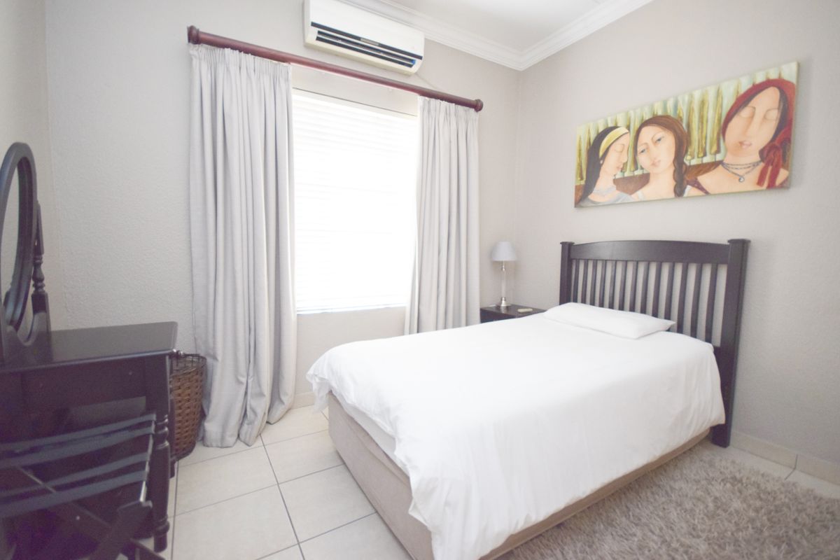 A well-maintained bedroom featuring tiled flooring, a wall-mounted air conditioning unit, and neutral wall finishes.
