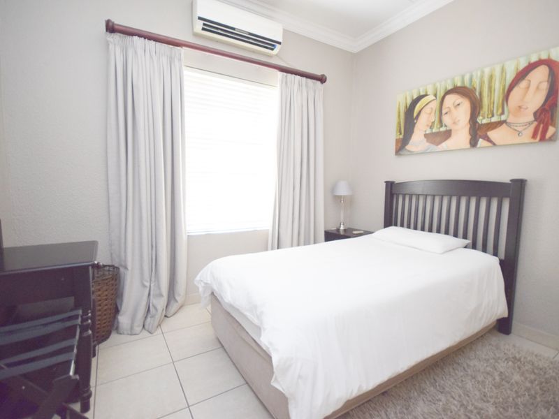 A well-maintained bedroom featuring tiled flooring, a wall-mounted air conditioning unit, and neutral wall finishes.