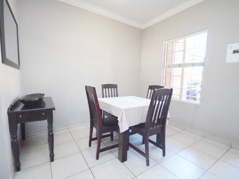 A simple dining area featuring neutral tiled flooring, a window with security bars, and classic cove cornice detailing.