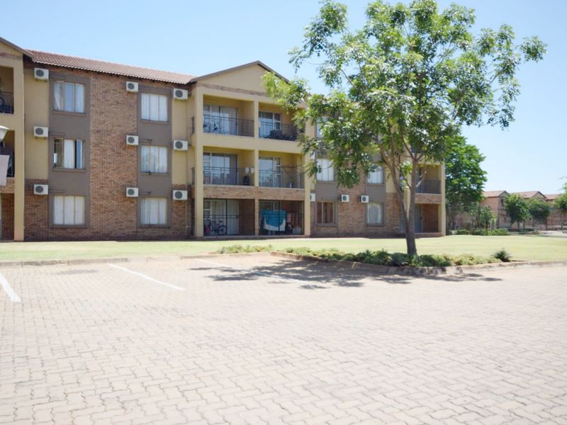 Exterior view of a multi-story brick apartment complex featuring private balconies, external air conditioning units, and a paved parking area.