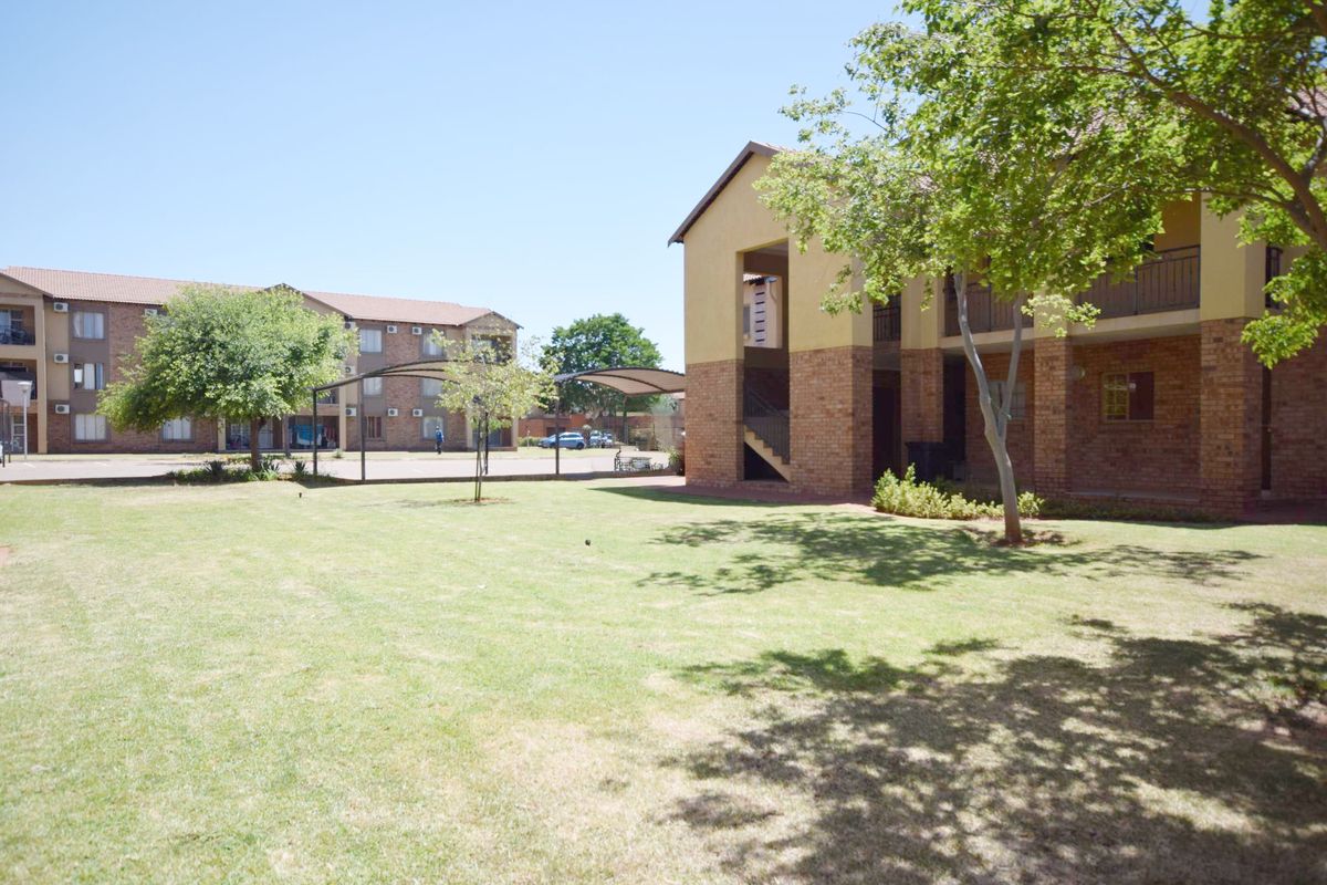 A view of the apartment complex grounds featuring brick buildings, landscaped lawn areas, and covered parking bays.