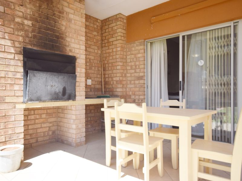 Covered patio area featuring a built-in brick braai and direct access to the interior through sliding glass doors.