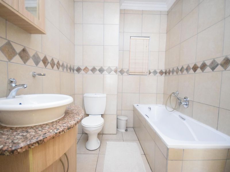 A functional bathroom featuring a vanity with granite countertop, vessel sink, toilet, and a tiled bathtub area with wall-mounted fixtures.