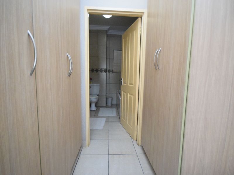 A hallway featuring built-in cupboards with light wood finish, leading into a tiled bathroom area.