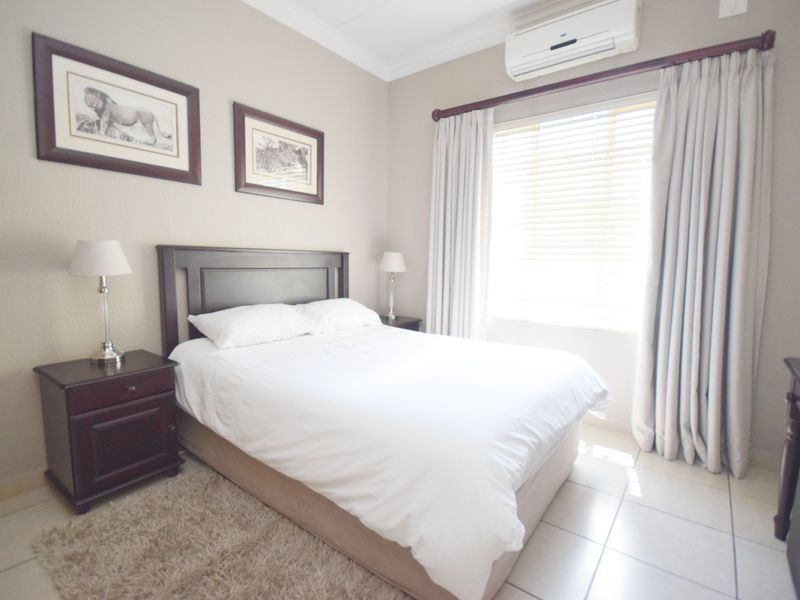 A well-maintained bedroom featuring tiled flooring, an integrated air conditioning unit, and window treatments including blinds and curtains.