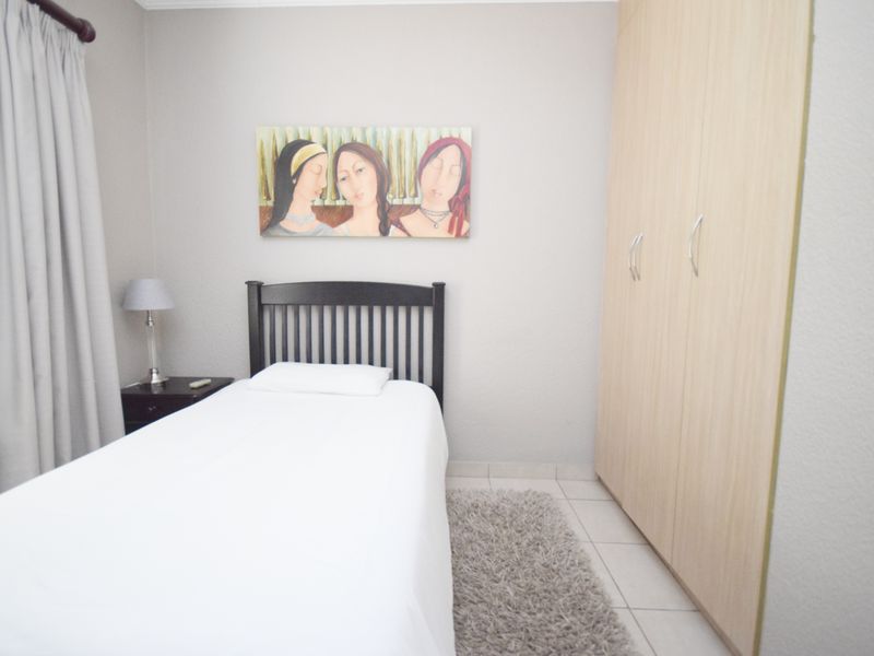 A well-maintained bedroom featuring neutral wall tones, tiled flooring, and a functional built-in wardrobe for storage.