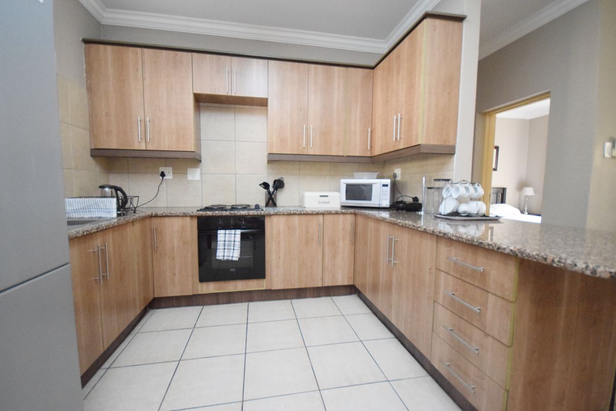 A functional kitchen featuring light wood-finish cabinetry, granite countertops, a tiled backsplash, and built-in oven with gas hob.