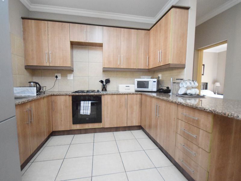 A functional kitchen featuring light wood-finish cabinetry, granite countertops, a tiled backsplash, and built-in oven with gas hob.