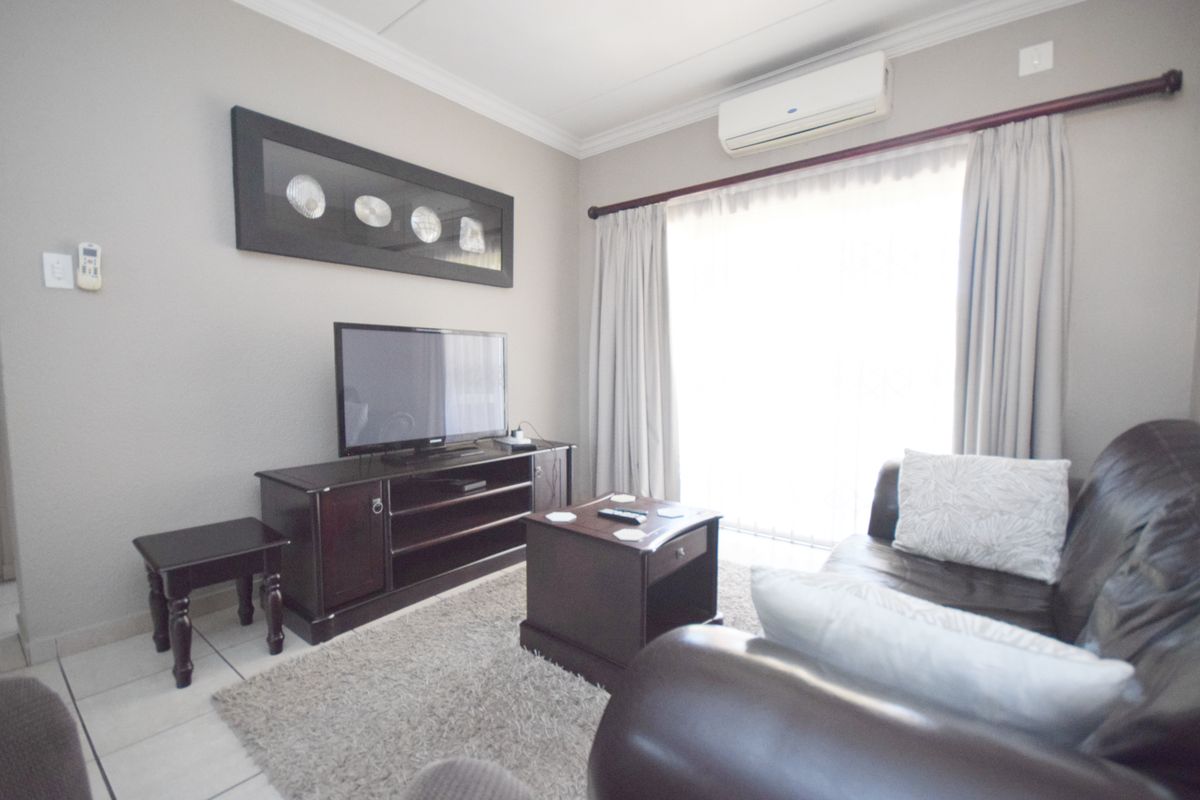 A comfortable living room featuring tiled flooring, a wall-mounted split-system air conditioner, and a sliding glass door providing natural light.