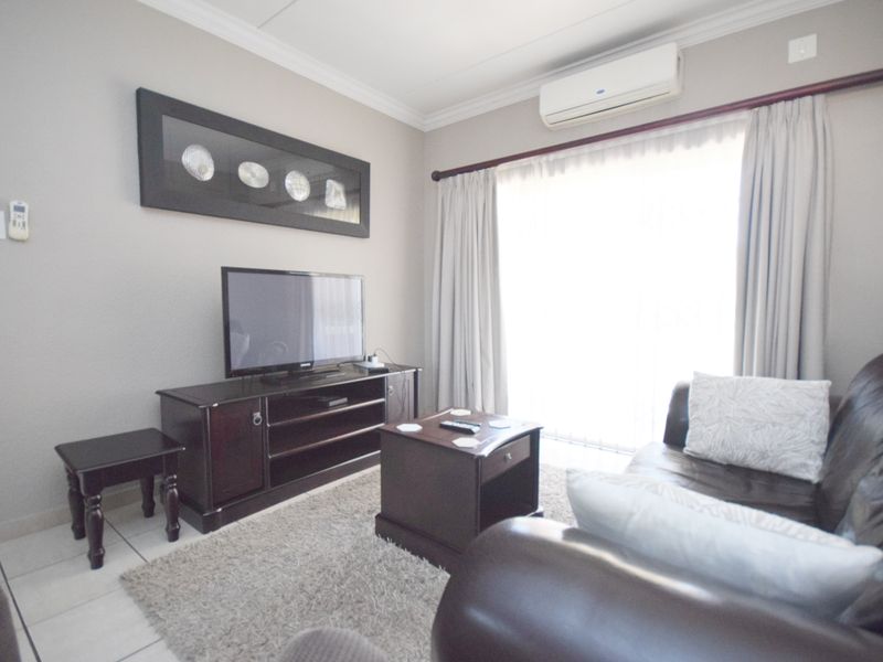 A comfortable living room featuring tiled flooring, a wall-mounted split-system air conditioner, and a sliding glass door providing natural light.