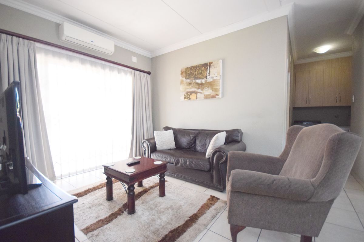 A comfortable living room featuring tiled flooring, crown molding, and a wall-mounted split-system air conditioner, with direct access to an outdoor area.