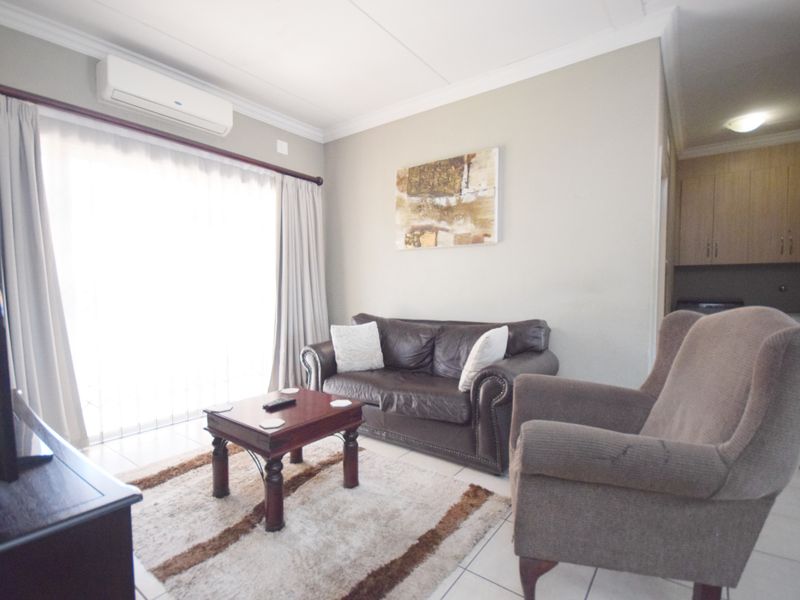 A comfortable living room featuring tiled flooring, crown molding, and a wall-mounted split-system air conditioner, with direct access to an outdoor area.