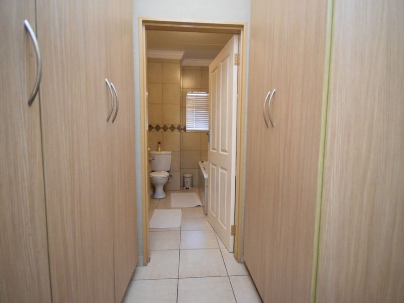 A hallway featuring built-in wooden cupboards leading into a tiled bathroom with a toilet and bathtub.
