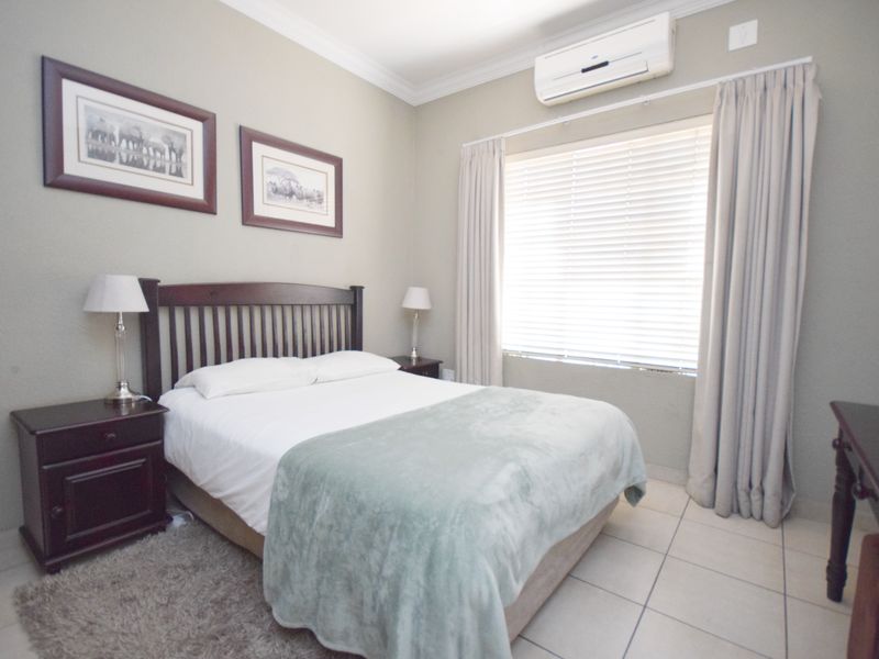 A well-maintained bedroom featuring tiled flooring, neutral wall tones, and a wall-mounted split-system air conditioner for climate control.