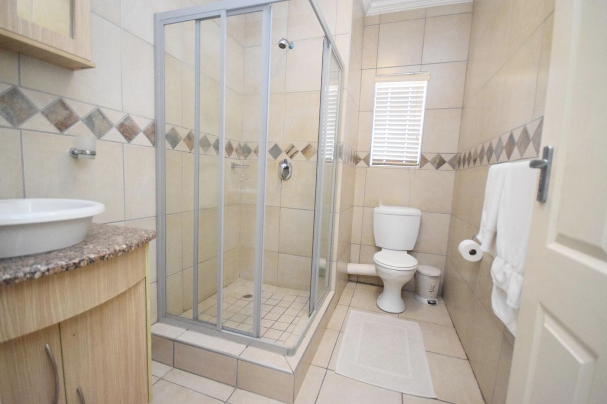 A functional bathroom featuring a glass-enclosed shower, a vanity with a vessel sink, and neutral wall and floor tiling.