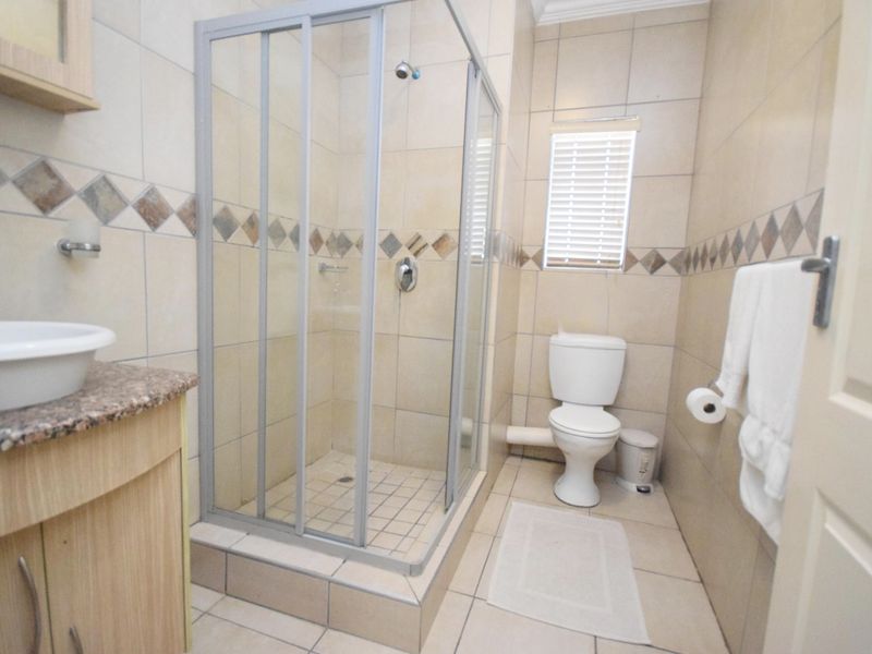 A functional bathroom featuring a glass-enclosed shower, a vanity with a vessel sink, and neutral wall and floor tiling.
