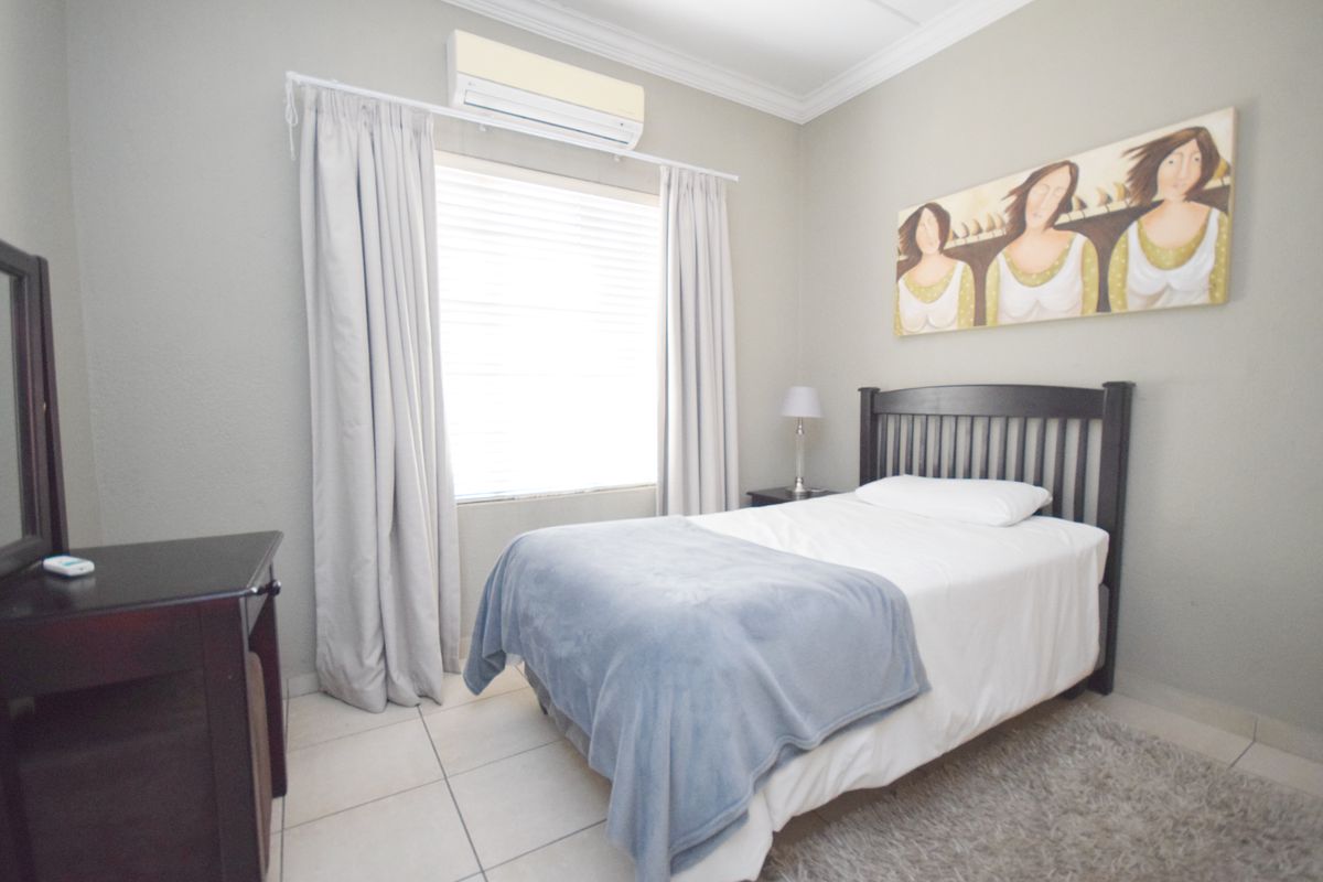 A well-maintained bedroom featuring neutral wall tones, tiled flooring, and a wall-mounted split-system air conditioning unit.